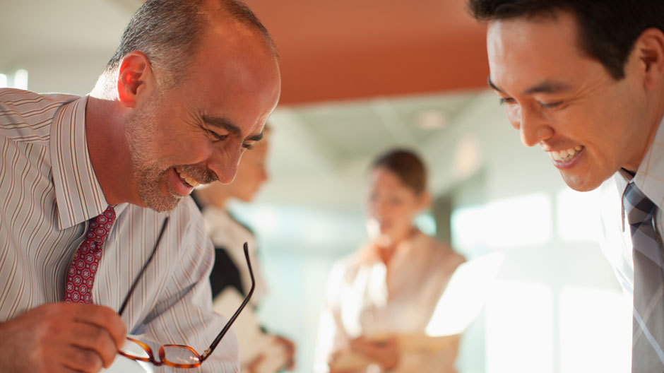 Two office workers laughing as they discuss a work topic