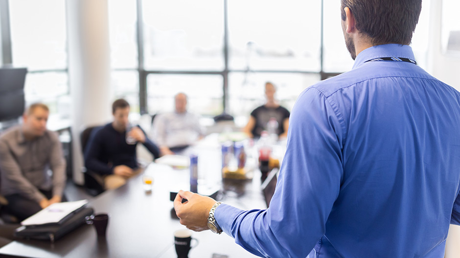 A man explaining in front of people in a meeting